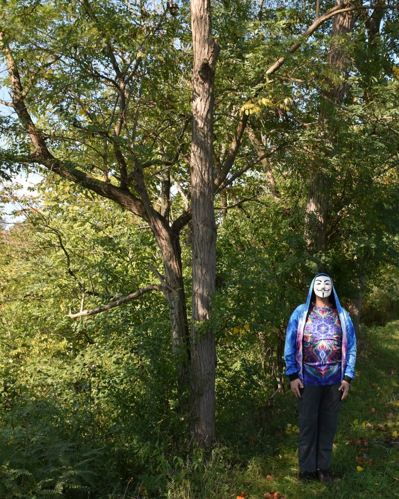 Joe in Guy Fawes mask standing in woods.